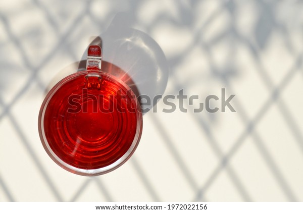 Slimming tea. Hibiscus tea diet. Sunlight\
through the screen creates light and shadow on a nude color\
background. Glass cup and red beverage in composition. Copy space.\
Sunny day. Weight loss\
concept.
