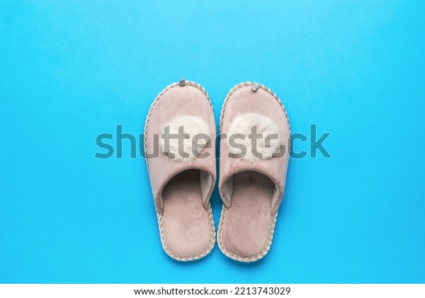 Slippers for home with fur trim on a\
blue background. The concept of home shoes. Flat\
lay.