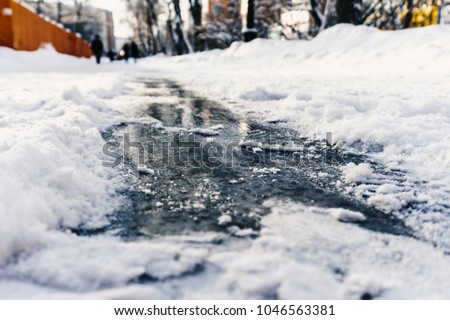 Slippery shiny ice on the sidewalk in winter under the snow beckons to ride on it to enjoy