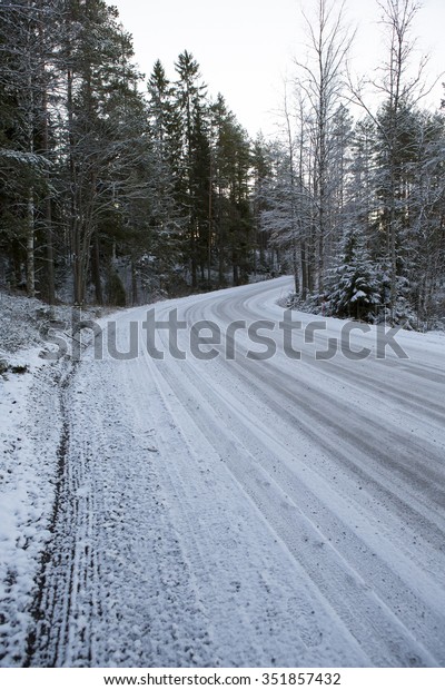 Slippery and snow road curving right on a cold\
winter morning. Image taken during sunrise after the first snow\
covered up the ground. It\'s mandatory to wear winter tires in\
Finland in winter\
time.