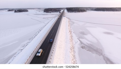 Slippery winter country road with bridge across frozen river. Karelia, Russia. Vehicles driving on highway. Aerial view
