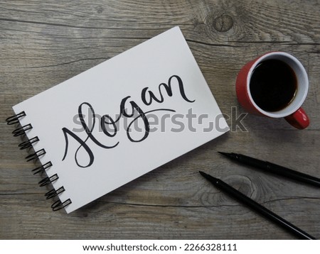 SLOGAN lettering in notepad with cup of coffee and pens