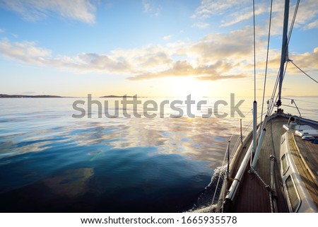 Sloop rigged modern yacht with wooden teak deck sailing at sunrise. A view from the deck to the bow. Colorful clouds. Port Ellen, Isle of Islay, Inner Hebrides, Scotland, UK
