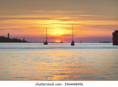 Sloop rigged yachts sailing near the lighthouse at sunset. Gulf of Riga, Baltic sea, Latvia. Golden sunlight, glowing clouds. Panoramic view. Transportation, cruise, regatta, tourism, leisure activity