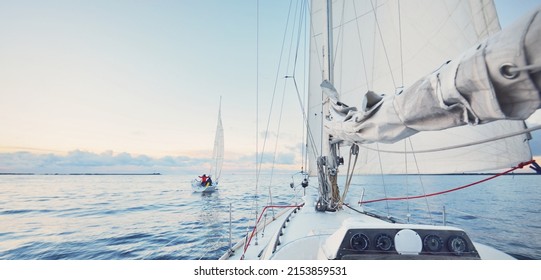 Sloop rigged yachts sailing in a still water at sunset. Frost and first snow on the deck, close-up view to the bow, mast, ropes and sails. Clear blue sky with colorful winter clouds. Norway - Powered by Shutterstock