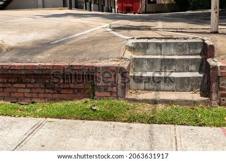 Sloping concrete parking lot ending at the top of a low brick retaining wall and cement block stairs to a sidewalk and grass, horizontal aspect ストックフォト © 