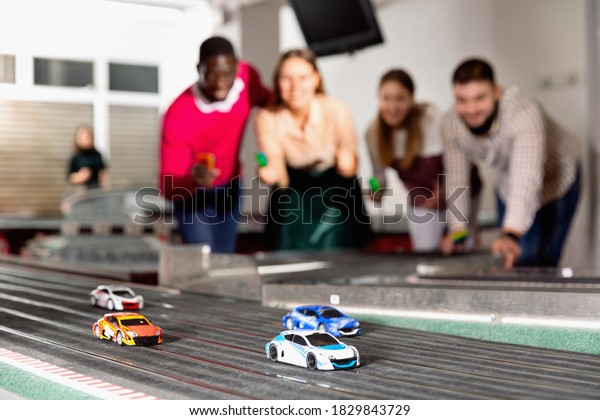 Slot car racing track. Emotional players drive\
toy cars in the background