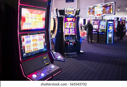 A slot machine is seen in a casino room with people playing other slot machines in the background. - Shutterstock ID 565543732