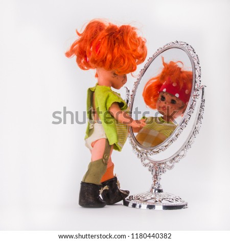 A slovenly little girl watching herself . Doll with red hair looks at herself in the mirror and playing with reflection.
