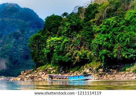 Slow boat cruise on the yellow  Mekong River in Laos, tropical jungle background