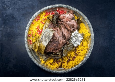 Slow cooked Omani lamb shuwa coated in rub of spices and wrapped in banana leaves served with rice and yoghurt as top view on a rustic oriental tray