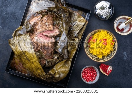 Slow cooked Omani lamb shuwa coated in rub of spices and wrapped in banana leaves served with rice and yoghurt as top view on a rustic metal tray 