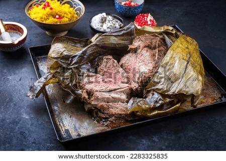 Slow cooked Omani lamb shuwa coated in rub of spices and wrapped in banana leaves served with rice and yoghurt as close-up on a rustic metal tray 