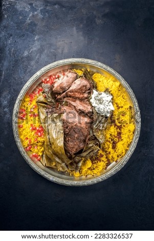 Slow cooked Omani lamb shuwa coated in rub of spices and wrapped in banana leaves served with rice and yoghurt as top view on a rustic oriental tray with copy space