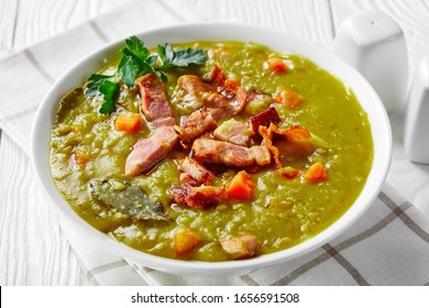 Slow Cooker German Split Pea Soup With Bacon, Pork Ham, Carrot, Potato, Thyme Served On A White Bowl With Ceramic Shakers On A White Wooden Background, Close-up