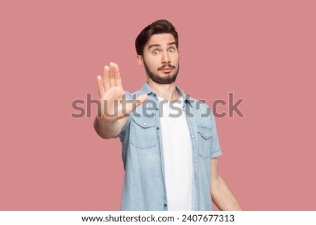 Slow down. Displeased bearded man shows stop gesture, asks to hold horses, keeps palms towards camera, says take it easy and control your behavior. Indoor studio shot isolated on pink background.