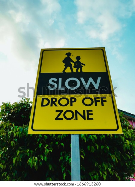 Slow down drop off zone warning yellow banner\
traffic sign at the school