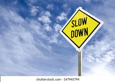 Slow Down yellow road sign on blue sky with clouds background
