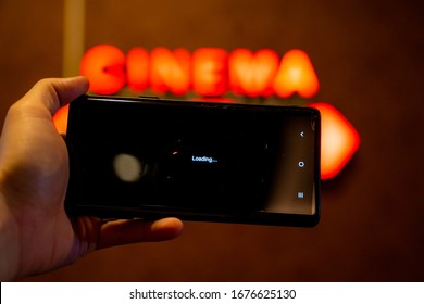 Slow Internet, Video Load And Download Speed. Watching Movie Online. Loading Icon On Screen.Hand With Black Empty Screen Mobile Phone . Background Red Wall With Cinema Signate.