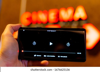 Slow Internet, Video Load And Download Speed. Watching Movie Online. Loading Icon On Screen.Hand With Black Empty Screen Mobile Phone . Background Red Wall With Cinema Signate.