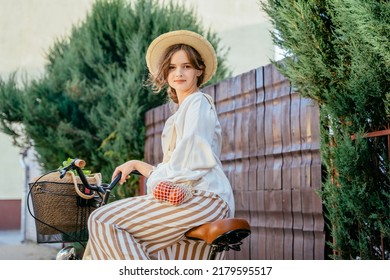 Slow living, simple village eco life. Portrait attractive woman in straw hat wearing linen clothes with wicker basket ride a bicycle at summer outdoor. Summer relaxing