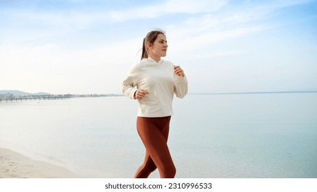 Slow motion of active and fit young woman running on the beautiful sandy beach, embodying the importance of physical activity and regular exercise