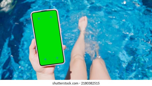 Slow Motion Of Asian Girl Wearing Hat Is Sitting On Edge Of Swimming Pool Kicking Feet Underwater In Rippled Clear Blue Water And Using Smartphone