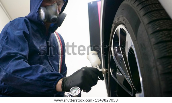 In slow motion\
a guy (man) professional in a garage in working form with sprays in\
the hands of a respirator and wearing protective glasses puts paint\
(ceramics) on car rims.