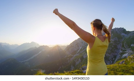 SLOW MOTION Happy woman raising her arms victoriously on rocky mountaintop at golden sunset. Hiking girl outstretching arms when reaching top of mountain at sunrise. Young trekker achieving daily goal