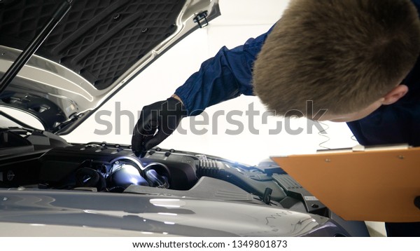 Slow Motion\
Man (Male) professional in working form and flashlight with a\
folder in his hands checks a car engine for serviceability. Concept\
of: Autocentre, Service,\
Diagnostics.