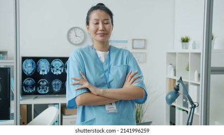 Slow Motion Portrait Of Young Asian Woman In Scrubs Standing In Hospital Office Smiling And Looking At Camera. Nurse And Workplace Concept.