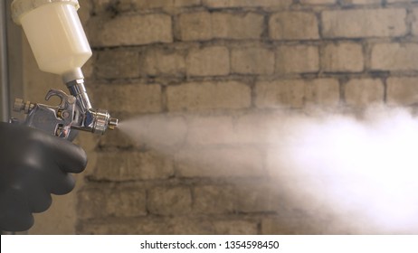 In Slow Motion A Professional Man (guy) In A Garage (service) In Working Clothes Dressed In A Sweater Sets Up A Paint Gun (spray Gun) And Starts Painting (putting A Layer Of Ceramics) A Yacht.