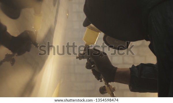In slow motion a professional man (guy) in a\
garage (service) in working clothes dressed in a sweater sets up a\
paint gun (spray gun) and starts painting (putting a layer of\
ceramics) a yacht.
