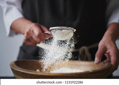 Slow motion shot of aged female hands sifting flour by sieve in wooden bowl.