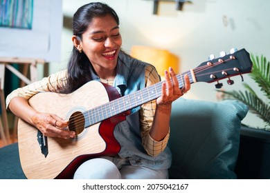 Slow motion shot of Happy Women enjoy singing by playing Guitar while sitting on sofa at home - Concept of Learning, practicing Guitar as hobby and Relaxing. - Powered by Shutterstock