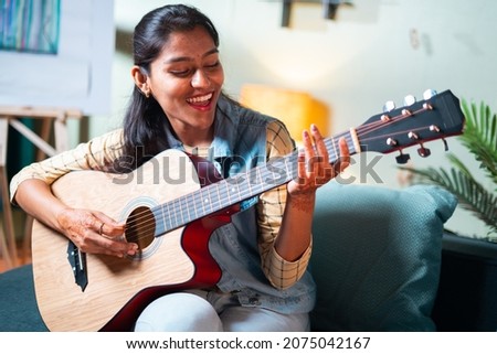 Slow motion shot of Happy Women enjoy singing by playing Guitar while sitting on sofa at home - Concept of Learning, practicing Guitar as hobby and Relaxing.