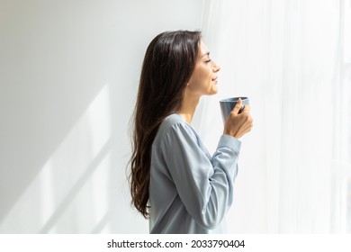 Slow motion Shot. Pretty young caucasian woman look at the scenery by the window and enjoying first morning coffee on sunshine. her enjoying pleasant memories. daily routine and relaxation time