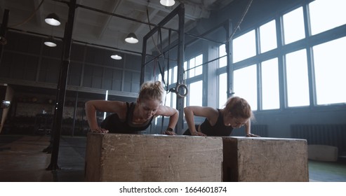 Slow Motion Two Young Beautiful Female Athletes Working Out, Doing Push-ups And Clapping Together In Atmospheric Gym.