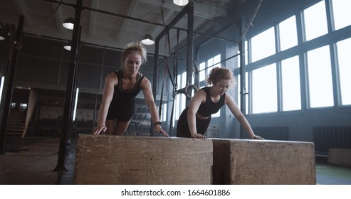 Slow Motion Two Young Beautiful Female Athletes Working Out, Doing Push-ups And Clapping Together In Atmospheric Gym.