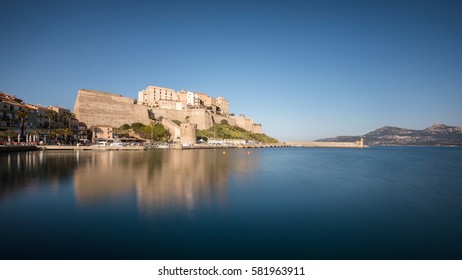 Slow shutter image of the citadel and harbour entrance at Calvi in the Balagne region of Corsica with clear blue sky and smooth calm waters