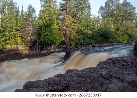 Slow shutter shot of a section of Temperance River with shore rocks in the foreground