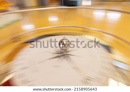 slow shutter speed and camera pan for blurred effect of a foucault pendulum along its path through a compass rose