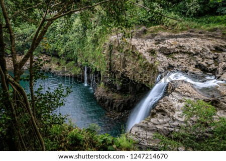 Slow shutter speed of a waterfall arching down into a deep green pool with lush tropical jungle on all sides at Rainbow Falls on the Big Island of Hawaii
