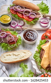 Slow-cooked Beef Sandwiches With Hoagie Rolls, Tomatoes, Cheese, Red Onion, Lettuce Leaves, Served With Mustard And Barbeque Sauce, On A White Wooden Background, Vertical Orientation, Close-up