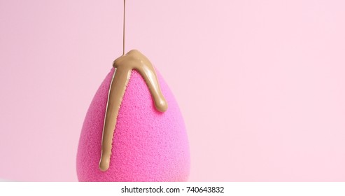 Slowly pouring liquid beige makeup foundation or bb cream on a clean pink sponge on light pink background