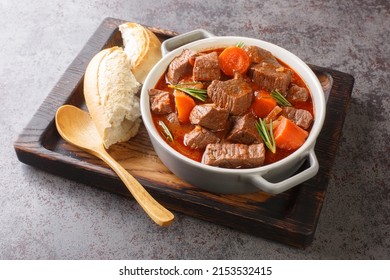 Slowly stewed spicy beef in red wine with vegetables closeup in the wooden tray on the table. Horizontal
