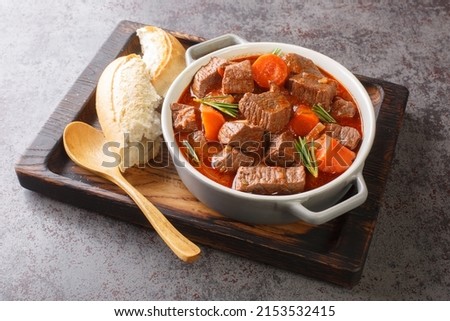 Slowly stewed spicy beef in red wine with vegetables closeup in the wooden tray on the table. Horizontal
