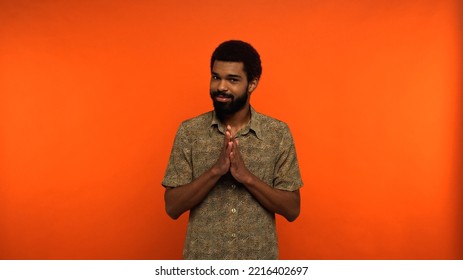 Sly African American Man With Beard Looking At Camera While Gesturing On Orange Background