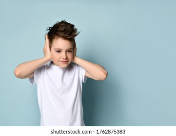 Sly Naughty Kid Smiling And Covering Ears With Hands Showing He Does Not Want To Hear And Obey. Facial Expression, Disobedient Child, Emotions, Childhood, Style. Studio Portrait Isolated On Light Blue