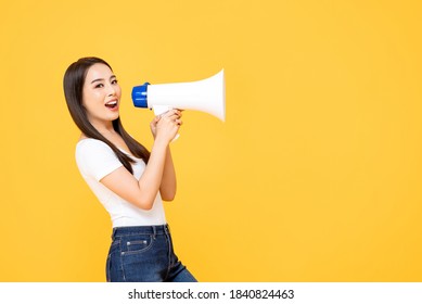 Smailing happy beautiful Asian woman announcing on magaphone isolated on yellow studio background with copy space